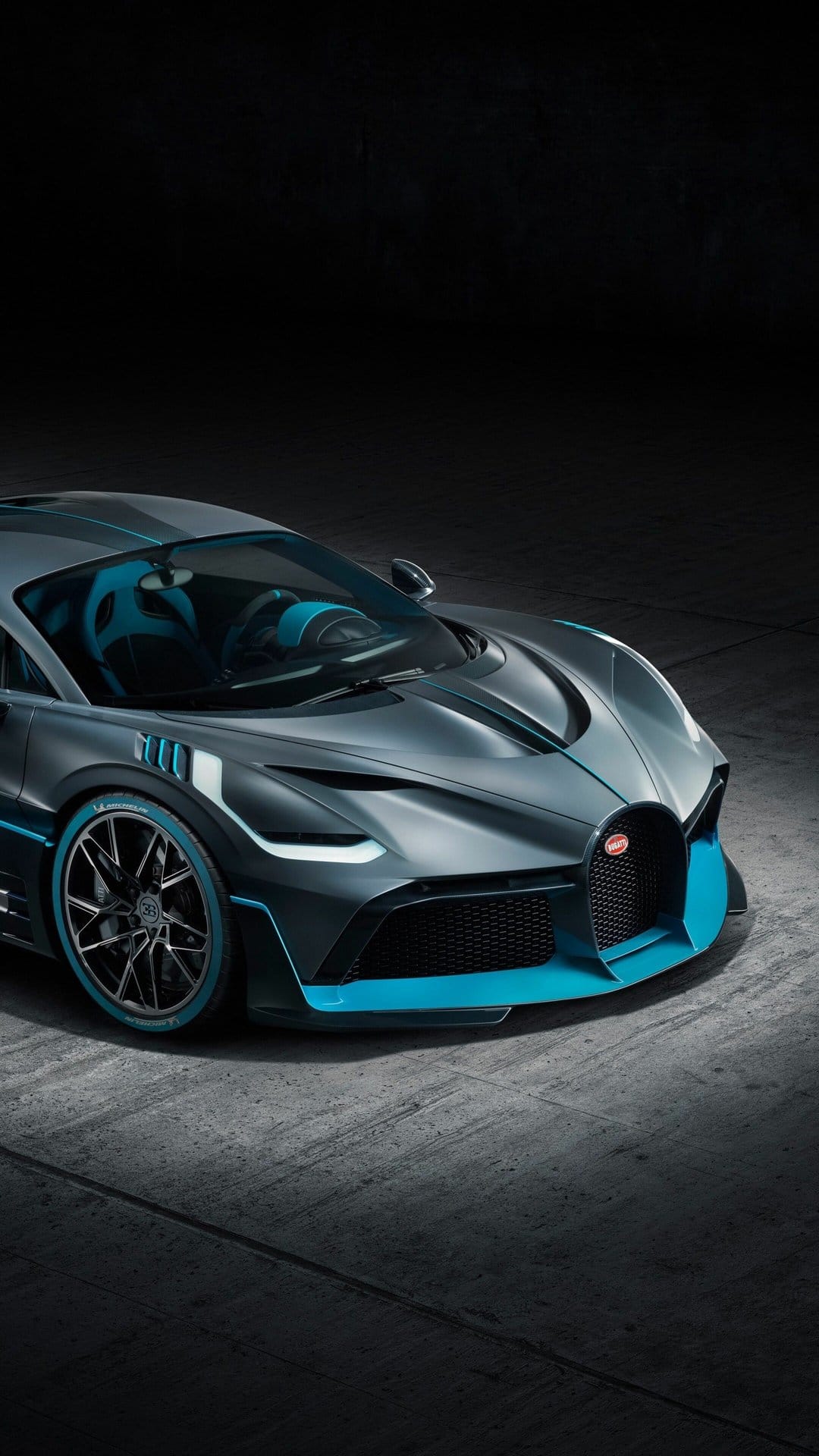 Matte grey Bugatti Divo hypercar with blue accents parked in a dark studio with dramatic lighting.