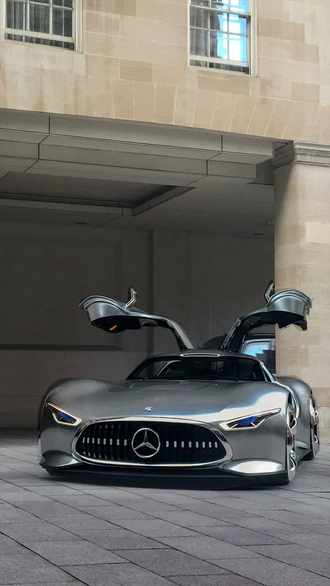 Silver Mercedes-Benz concept car with gullwing doors open against a backdrop of classical stone columns.