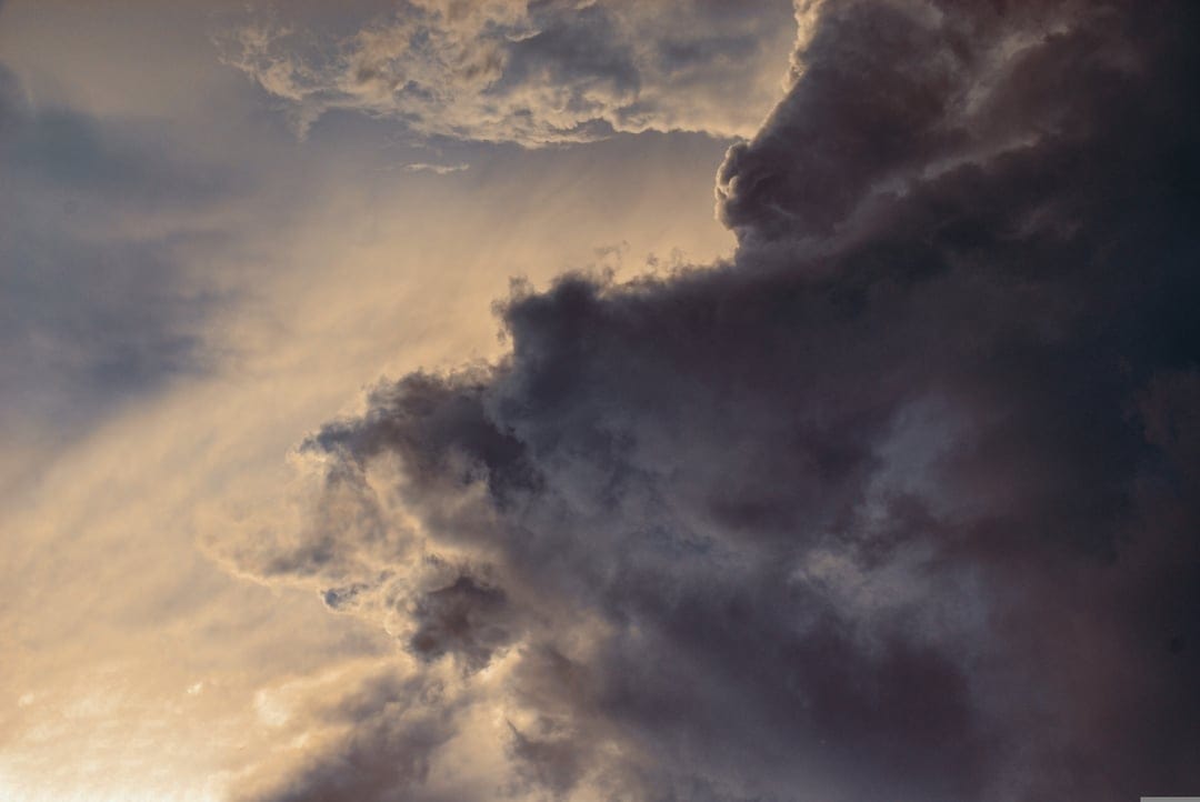 Dark storm clouds gather over a vibrant golden horizon during a dramatic sunset with heavy atmospheric contrast.