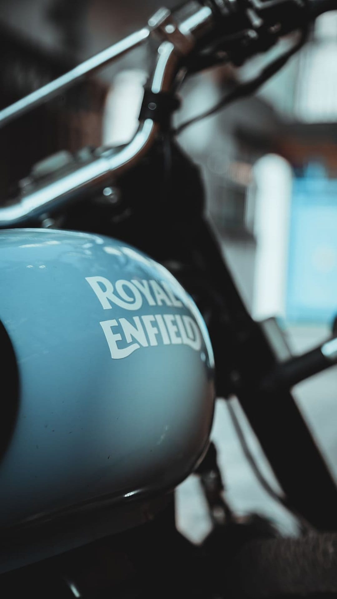 Royal Enfield teal fuel tank with white classic logo branding against a soft blurred out-of-focus background.