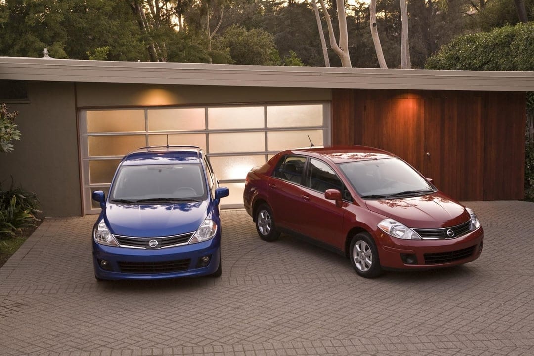 Blue and red Nissan cars parked on a brick driveway in front of a modern house with warm lighting at dusk.