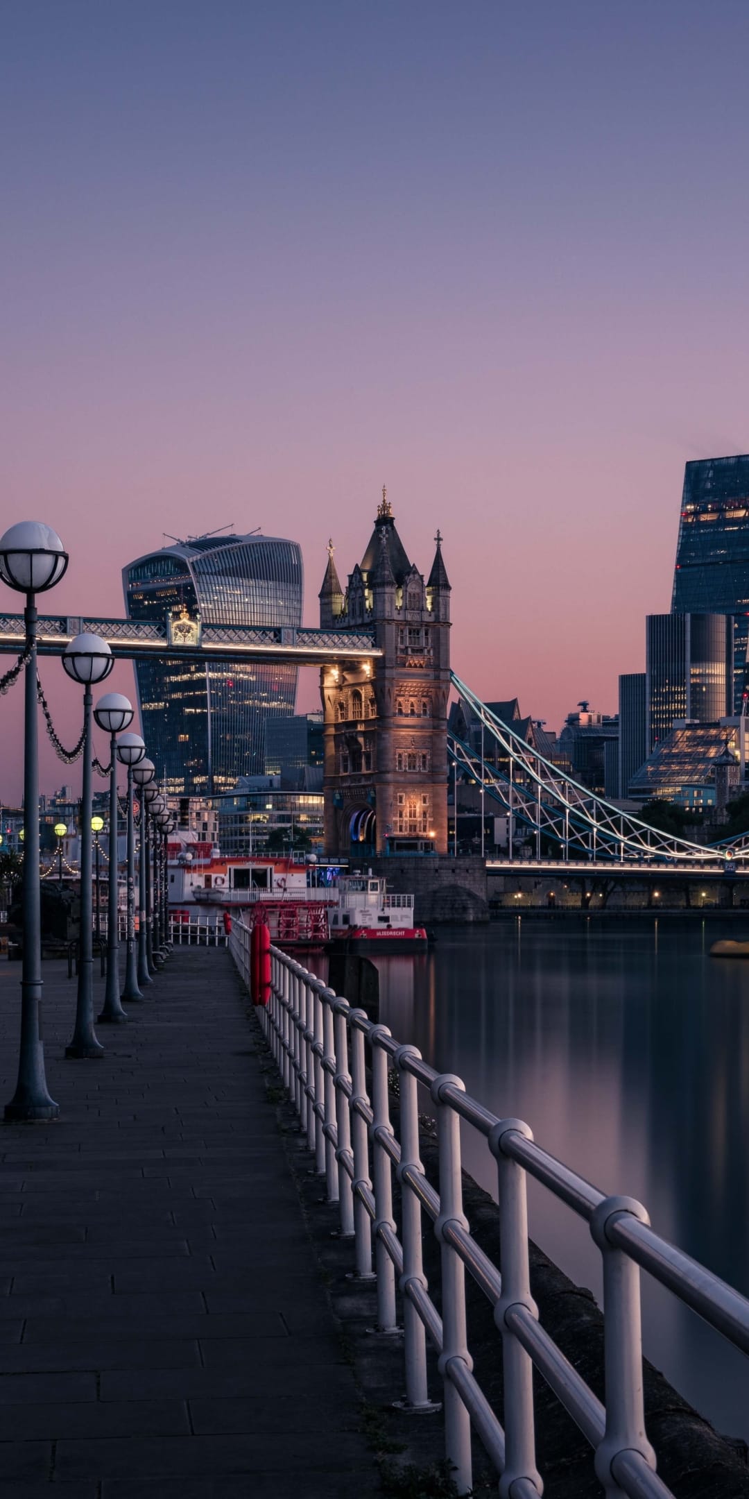Tower Bridge illuminated at dusk with blue and orange sky reflections on the River Thames water surface.