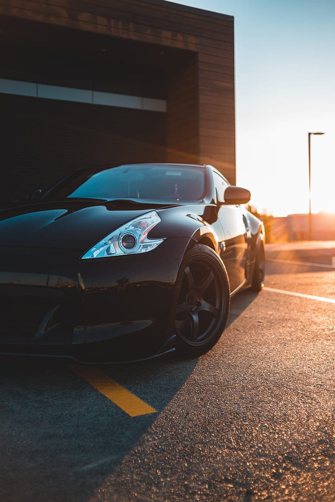 Black sports car parked near a modern building during sunset with warm reflections on its polished surface.