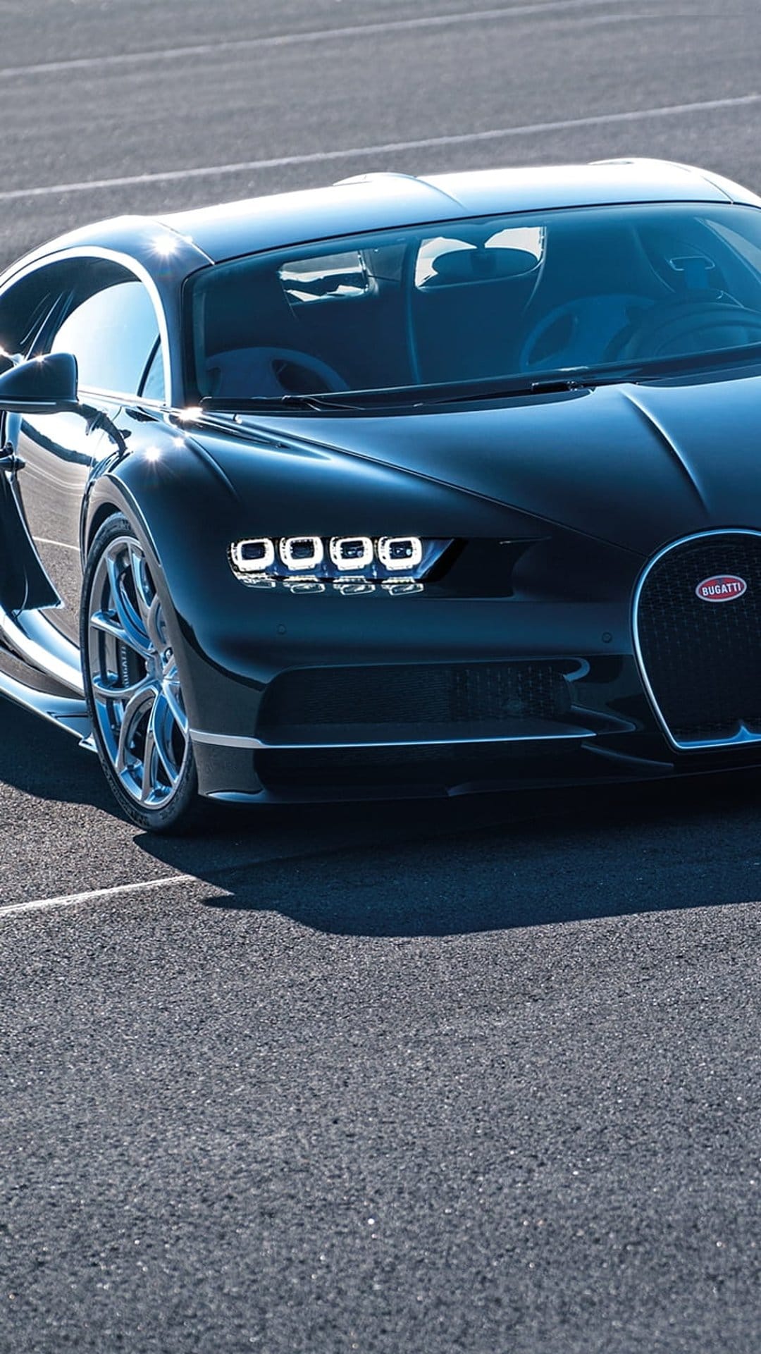 Bugatti Chiron hypercar with a black exterior and LED headlights parked on a sunlit asphalt road surface.