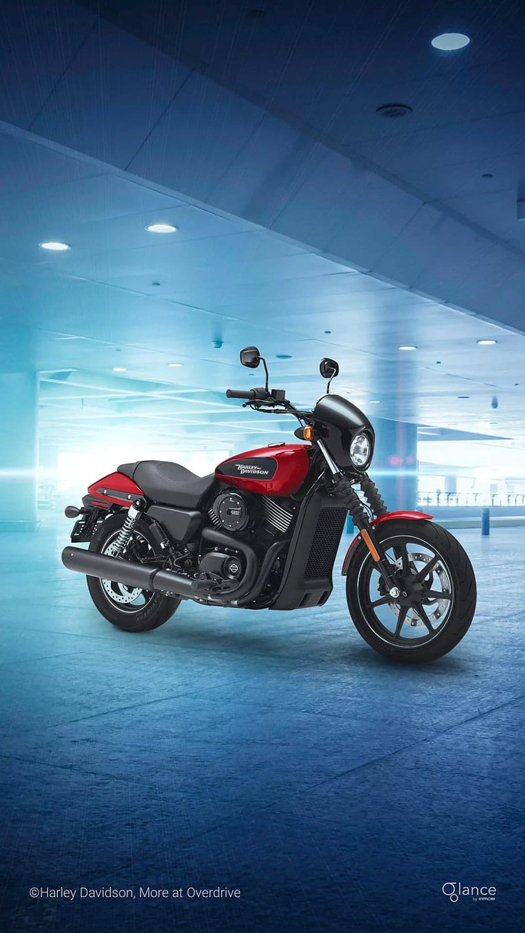 Red Harley Davidson Street 750 motorcycle with black engine parts parked in a modern blue-lit architectural room.