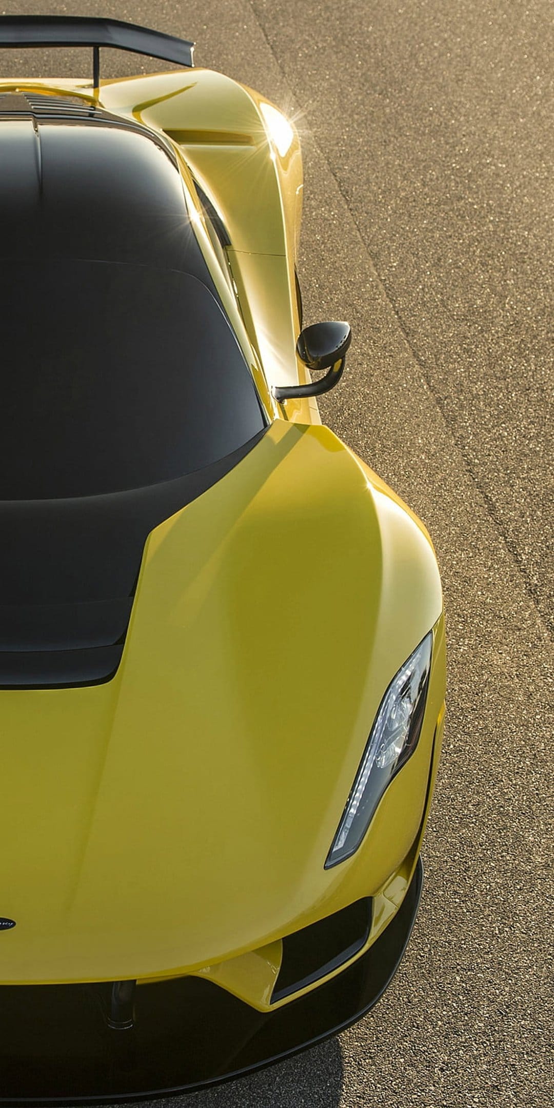 Yellow sports car headlight and spoiler with sunlight reflecting off its polished yellow paint on dark asphalt.