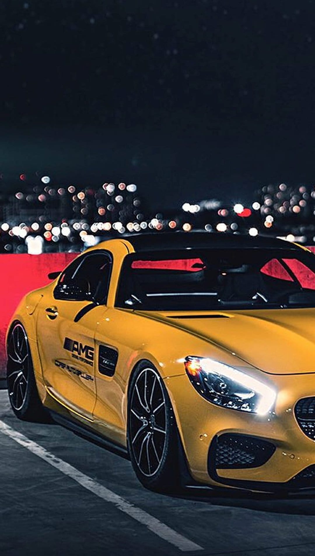 Yellow Mercedes-AMG GT sports car parked on an urban street at night with glowing headlights and bokeh lights.