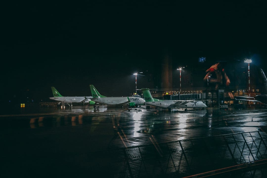 Commercial airplanes parked on a wet tarmac reflecting yellow floodlights against a dark midnight sky.