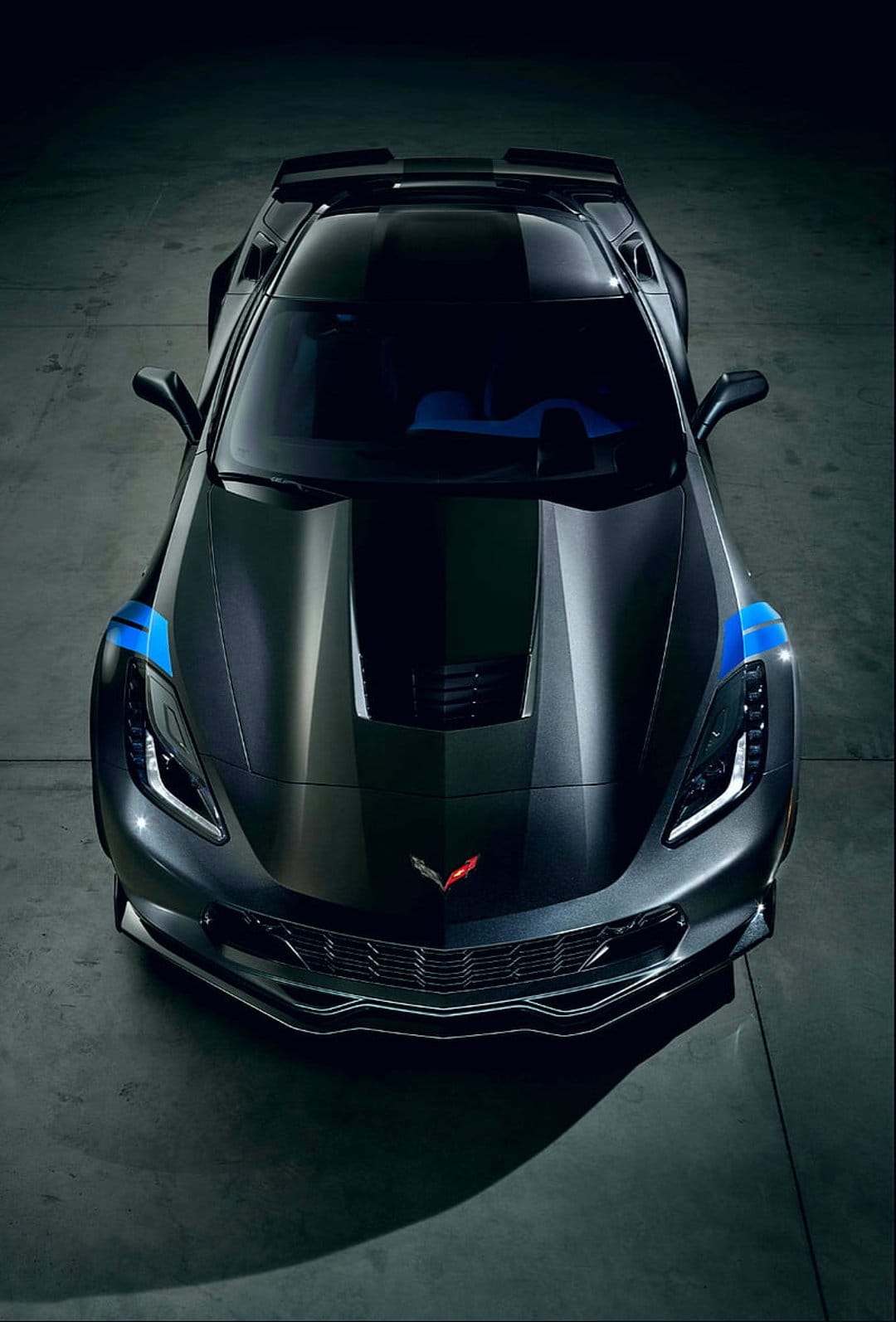 Dark gray Chevrolet Corvette C7 seen from above featuring vibrant blue racing stripes on the hood and roof.