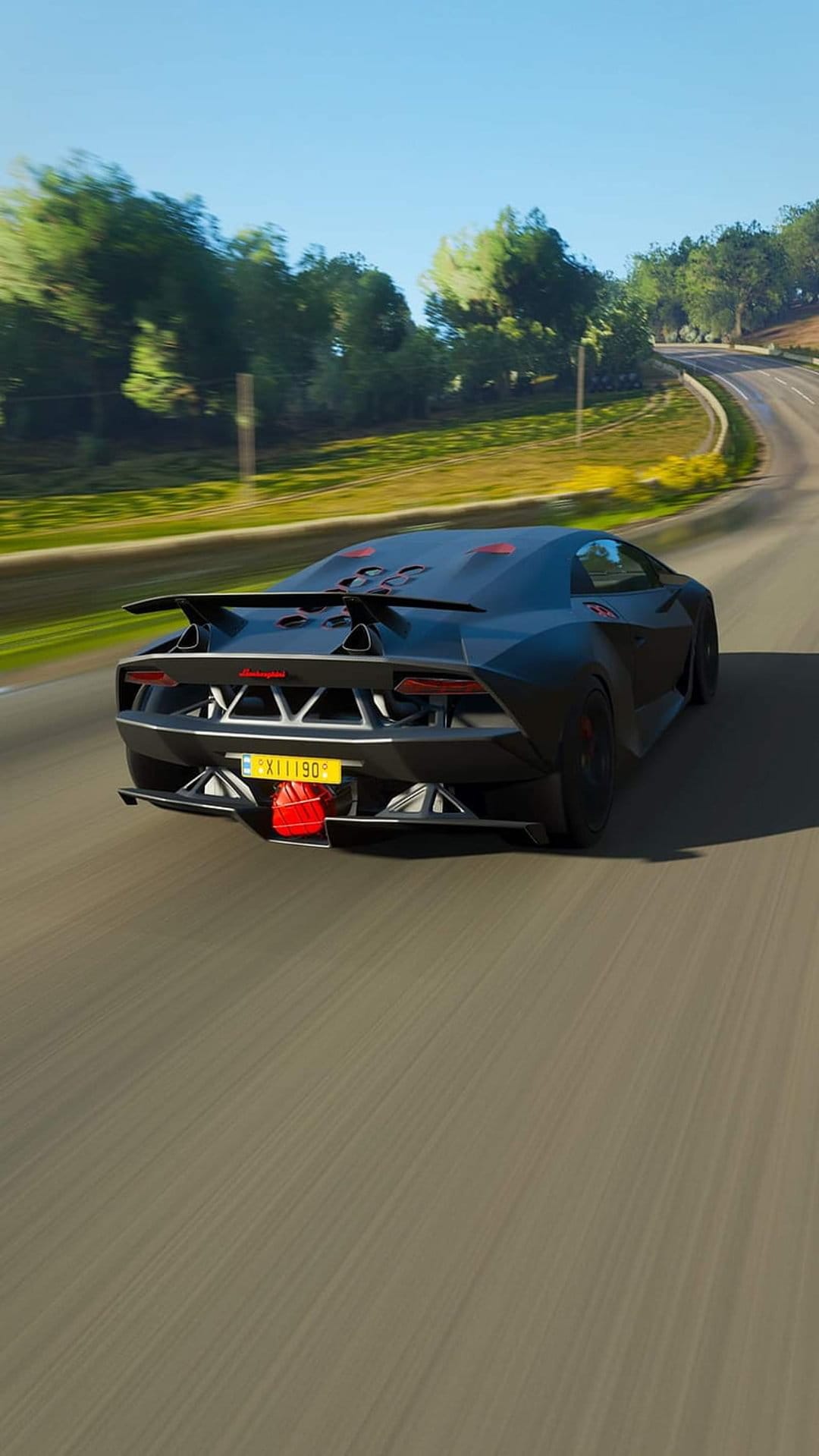 Black Lamborghini rear view showing angular taillights and a spoiler on a sunny highway with green trees.