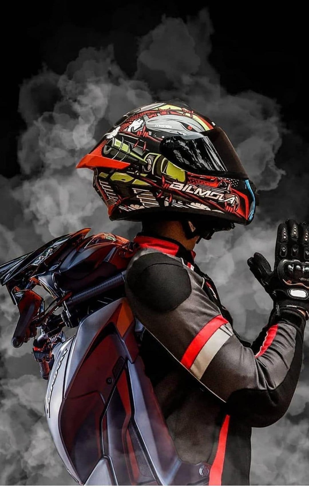 Motorcyclist wearing a futuristic red helmet and black racing suit with gloves raised amidst grey smoke.