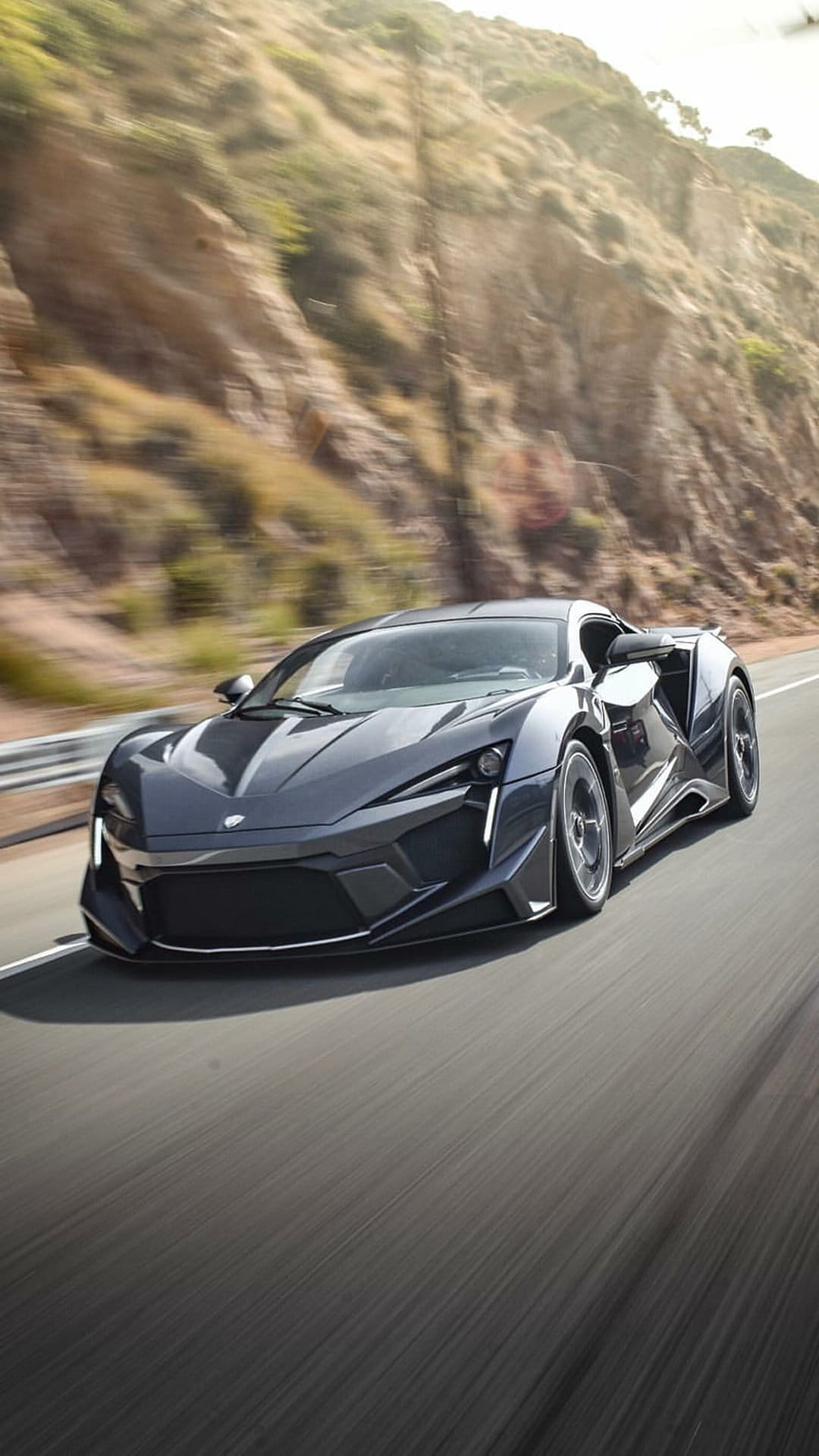 Lykan Hypercar speeding on a coastal road with motion blur, rugged cliffs, and golden sunlight in the background.