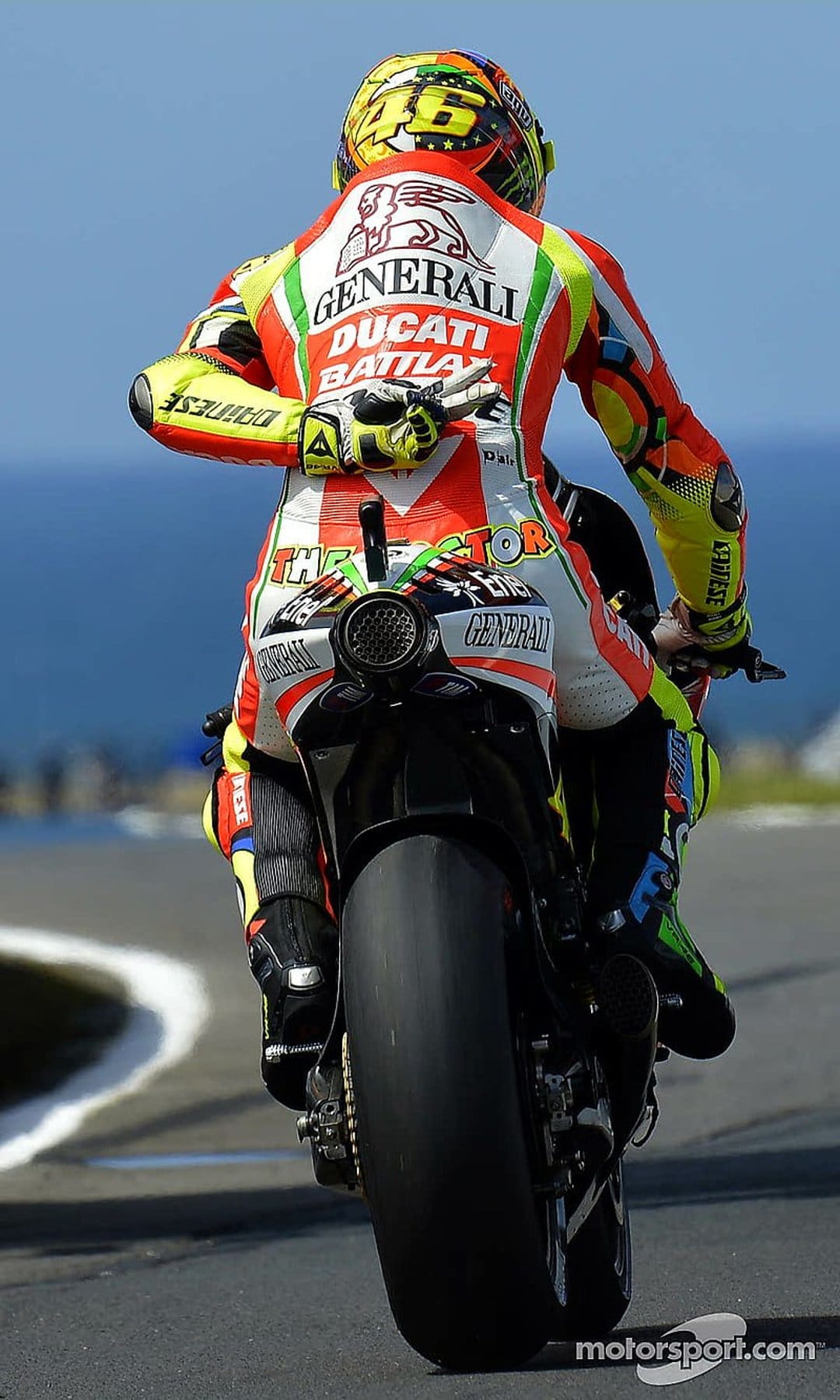 Valentino Rossi in yellow leathers rides a Ducati motorcycle on a track, focusing on the rear tire and exhaust.