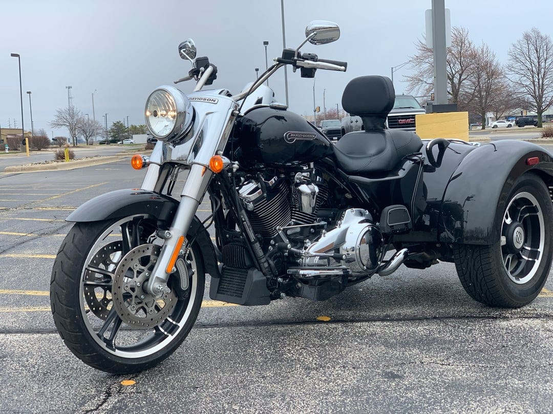 Black Harley-Davidson Freewheeler trike parked on asphalt with chrome details under a cloudy, overcast sky.