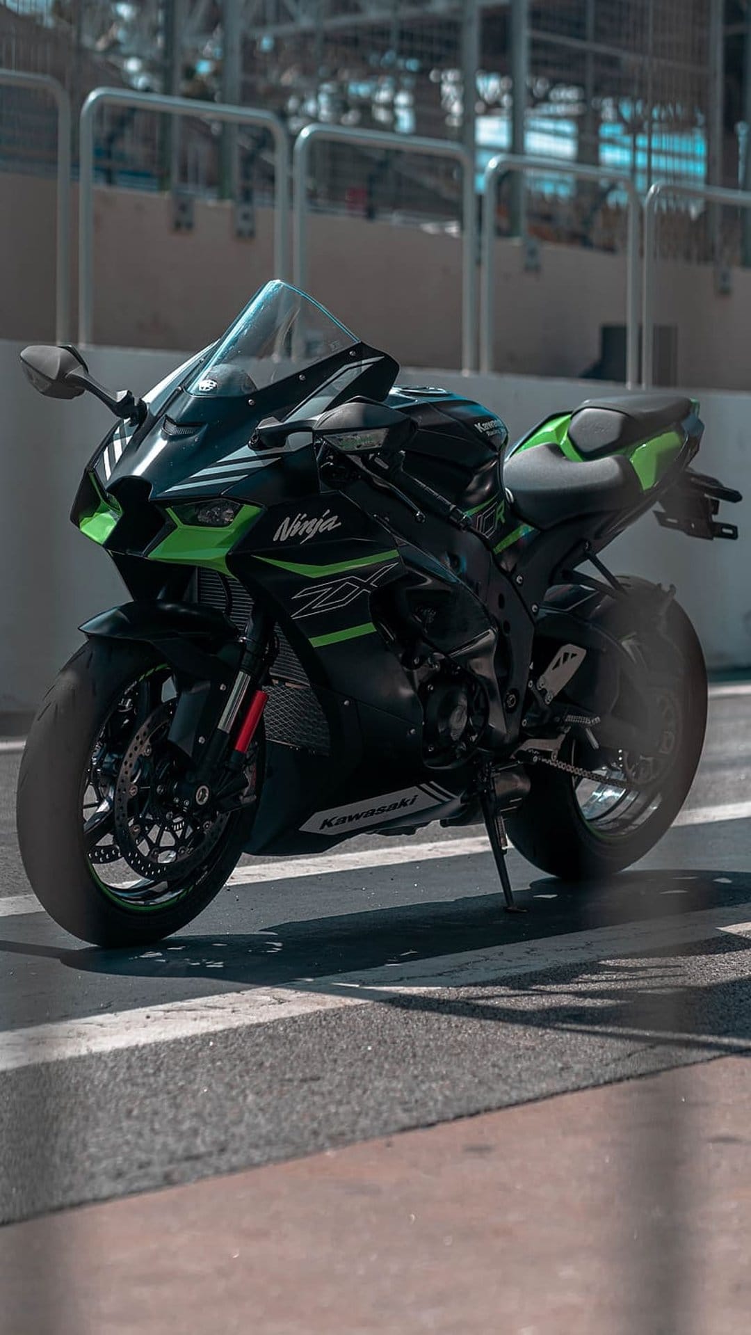 Kawasaki Ninja ZX-10R superbike with lime green accents parked on a paved racing circuit with blurred background.