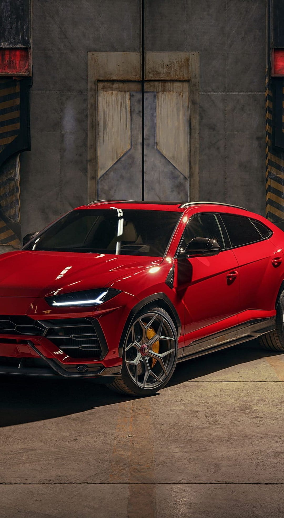 Red Lamborghini Urus SUV parked in a warehouse beside a large metal door with low-key industrial lighting.
