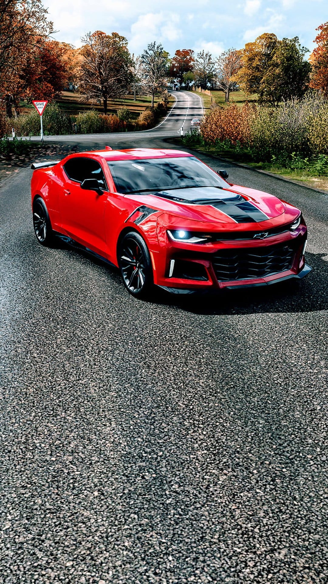 Red Chevrolet Camaro SS with black stripes driving on a wet road surrounded by orange autumn trees and a grey sky.