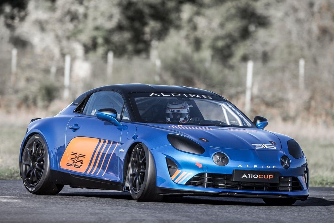 Blue Alpine A110 Cup racing car with orange number 36 graphics speeding on an asphalt track.