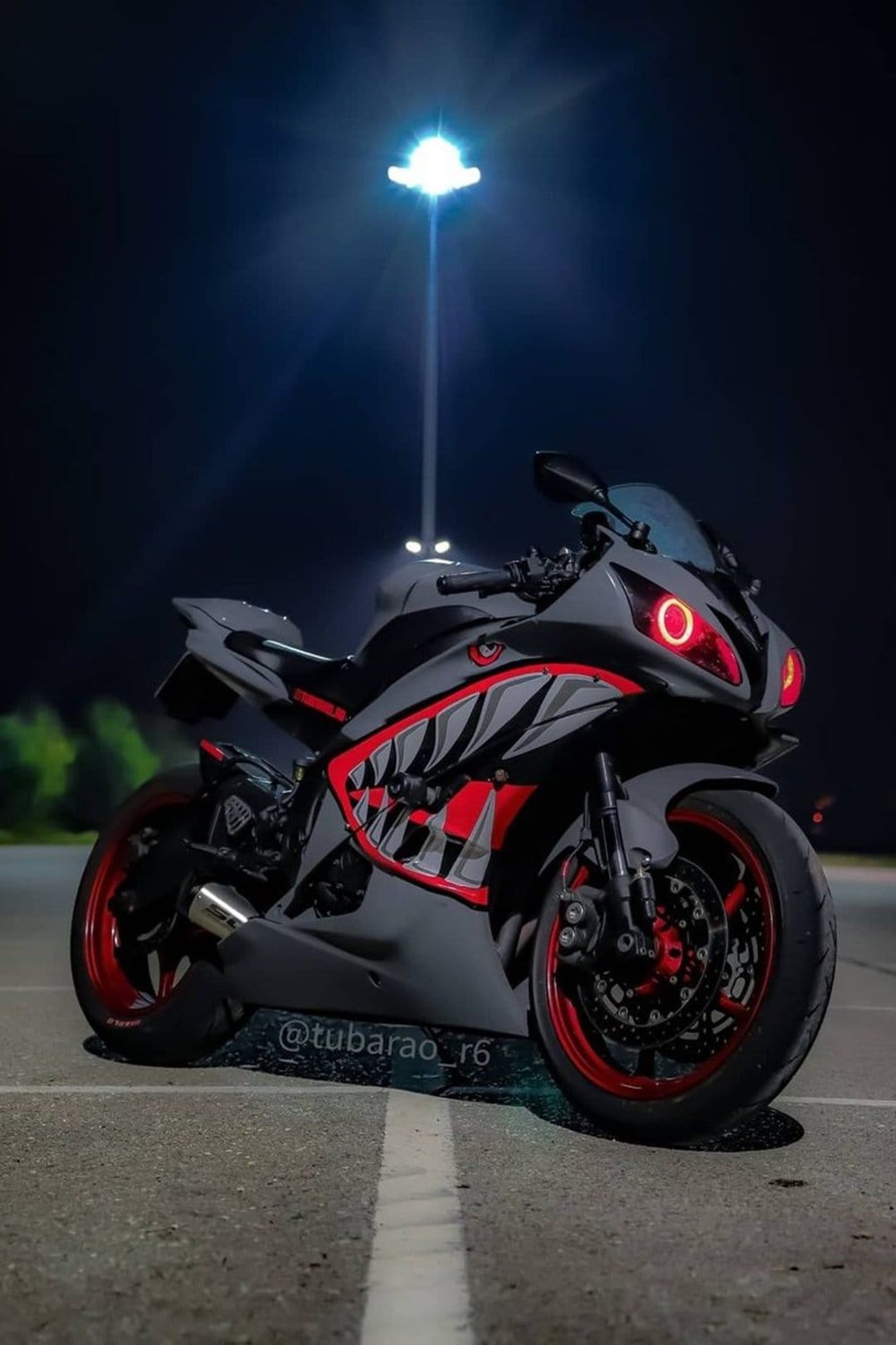 Custom Yamaha R6 motorcycle with shark decals and red halo headlights parked on asphalt under a night street lamp.