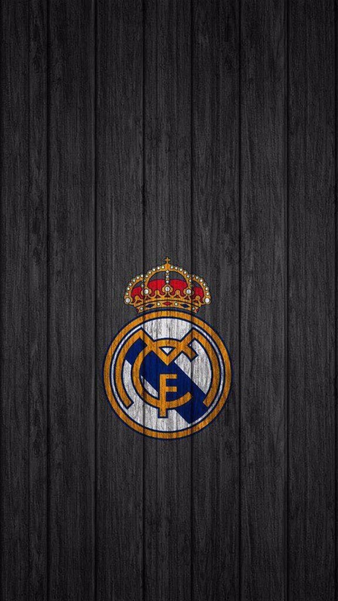 Real Madrid crest with a gold crown and blue accents centered on a dark, textured vertical wood grain surface.