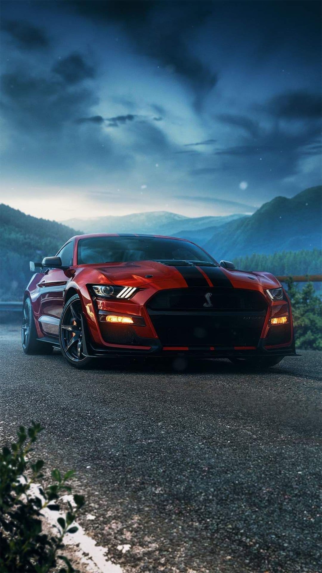 Red Ford Mustang Shelby GT500 with black stripes parked on a winding mountain road under a cloudy twilight sky.