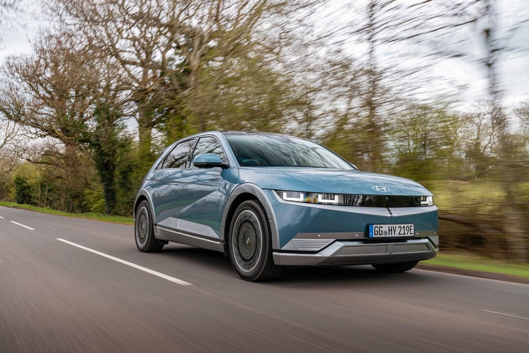 Blue Hyundai Ioniq 5 electric car driving on a rural road with motion blur and forest background.