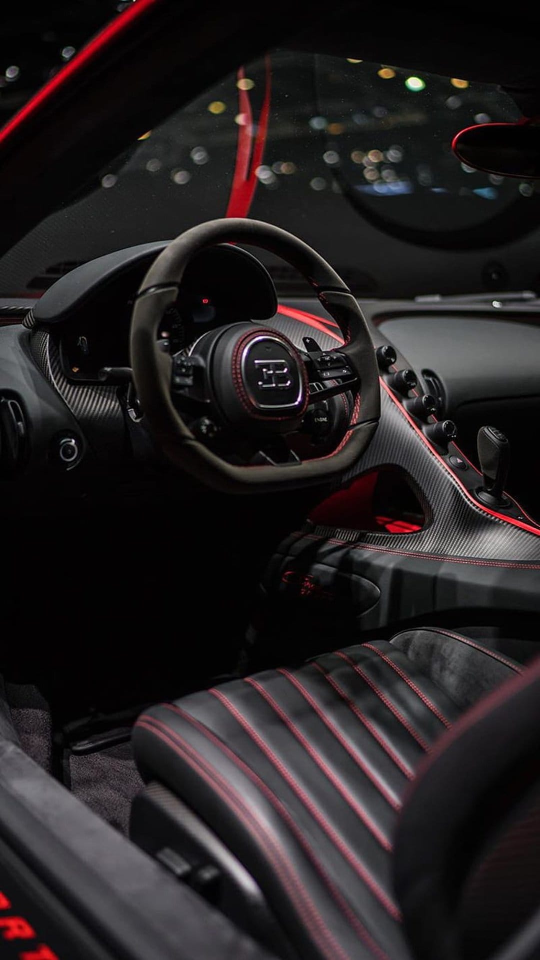 Bugatti steering wheel with a silver EB logo, red stitching on black leather, and carbon fiber dash details.