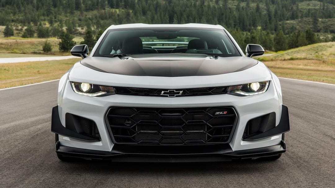 Front view of a white Chevrolet Camaro ZL1 1LE with black aero parts on a paved race track with forest background.