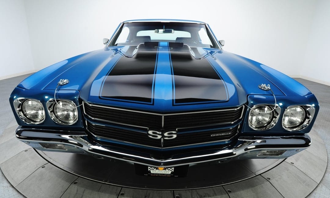 Front view of a blue 1970 Chevrolet Chevelle SS with black hood stripes and chrome bumpers in a white studio setting.