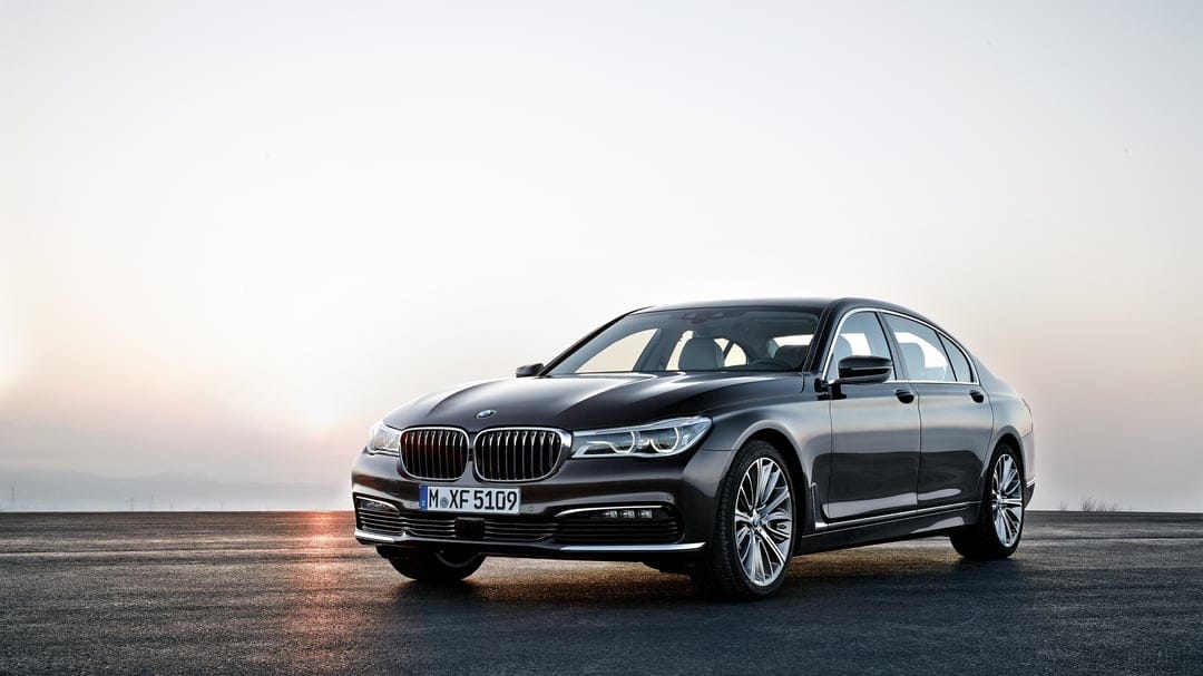Dark BMW 7 Series sedan parked on a flat road during a golden sunset with highlights on the chrome grille.