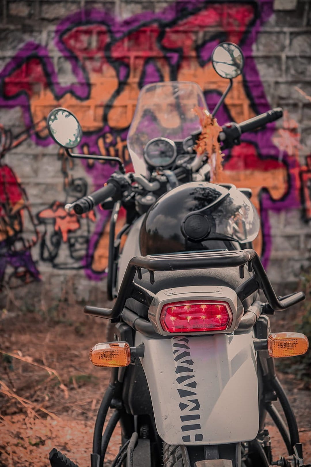 White motorcycle with a black helmet parked against a vibrant purple and orange graffiti-covered brick wall.