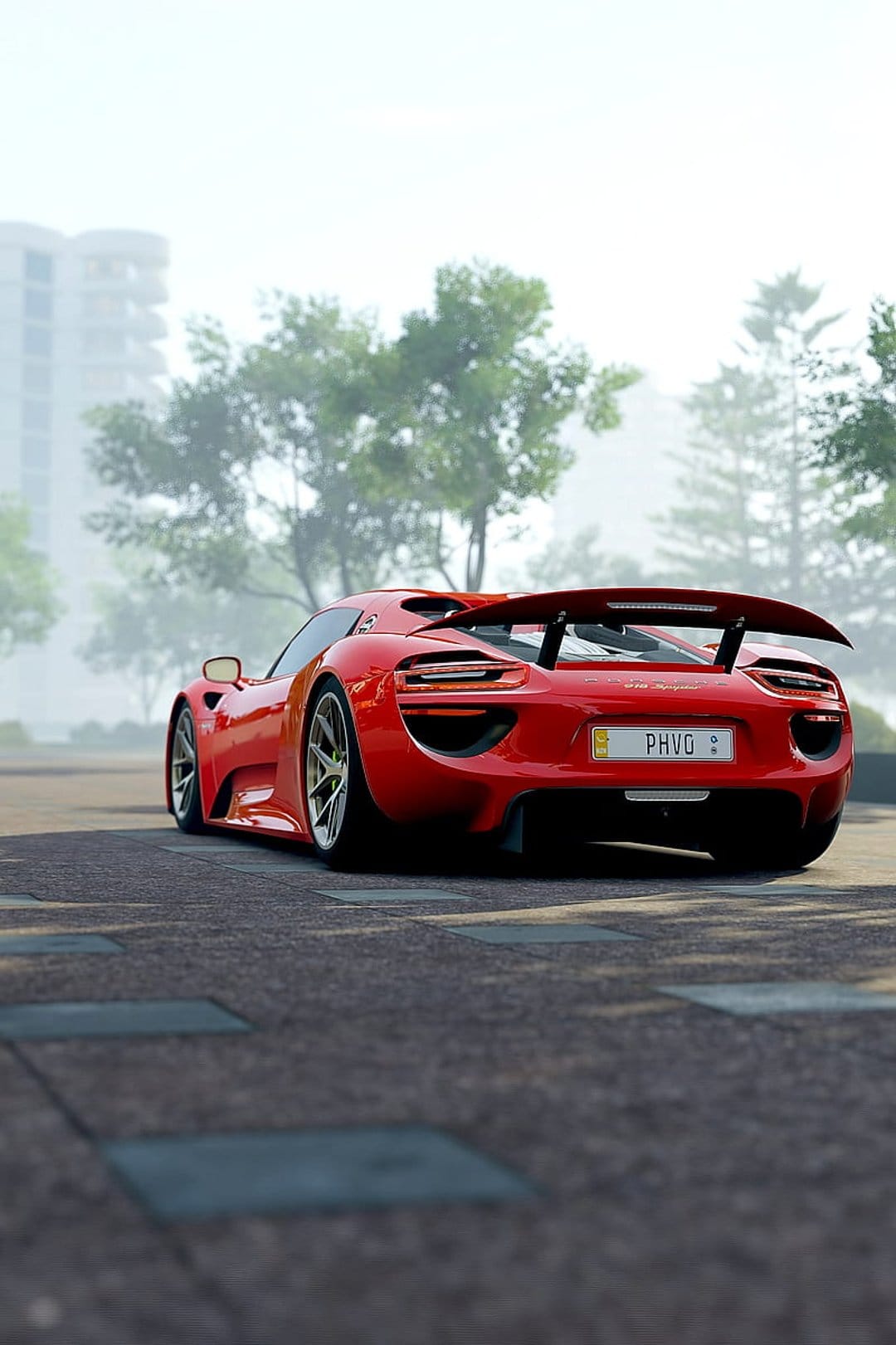 Porsche 918 Spyder rear showing the spoiler and license plate on a paved road with surrounding green trees.