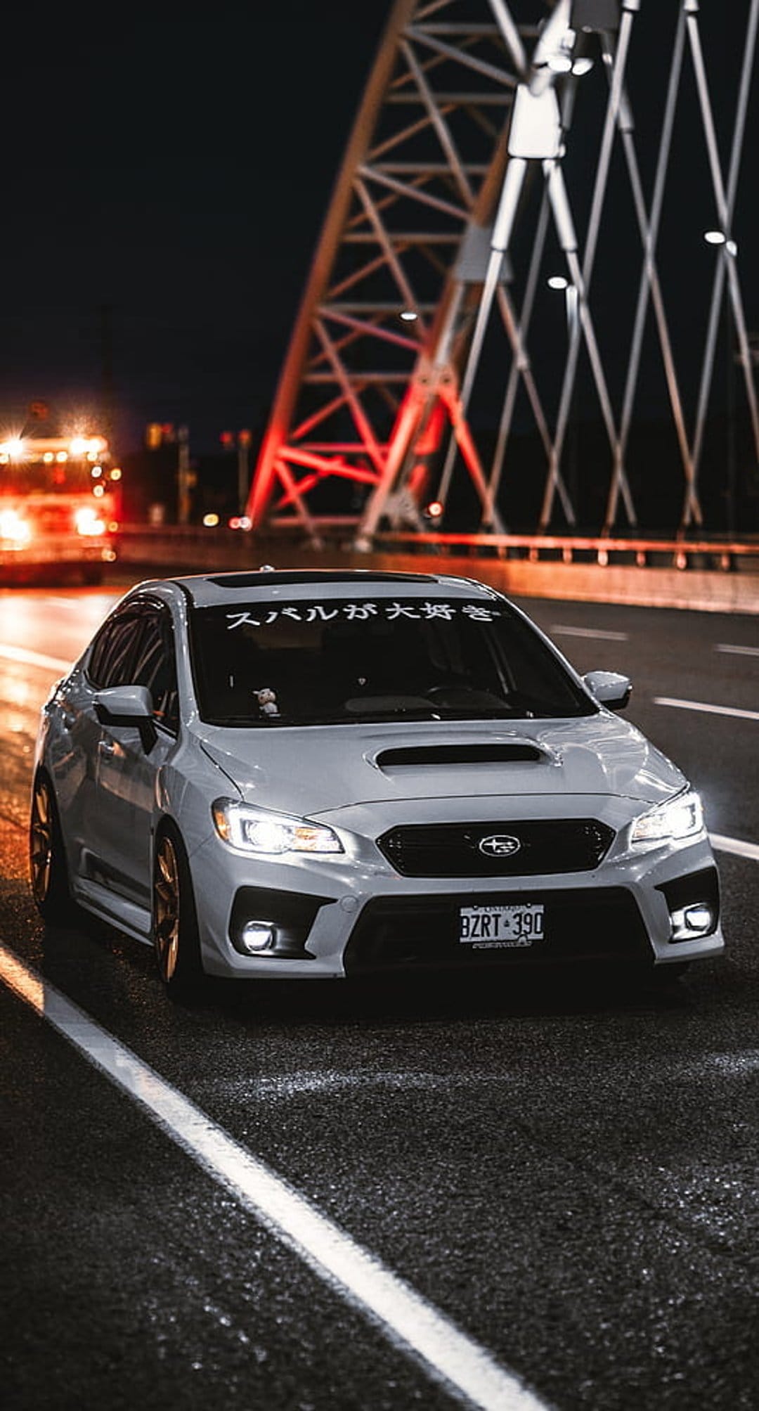 Gray Subaru WRX on wet asphalt under a bridge with red lights and glowing headlights in a moody night scene.