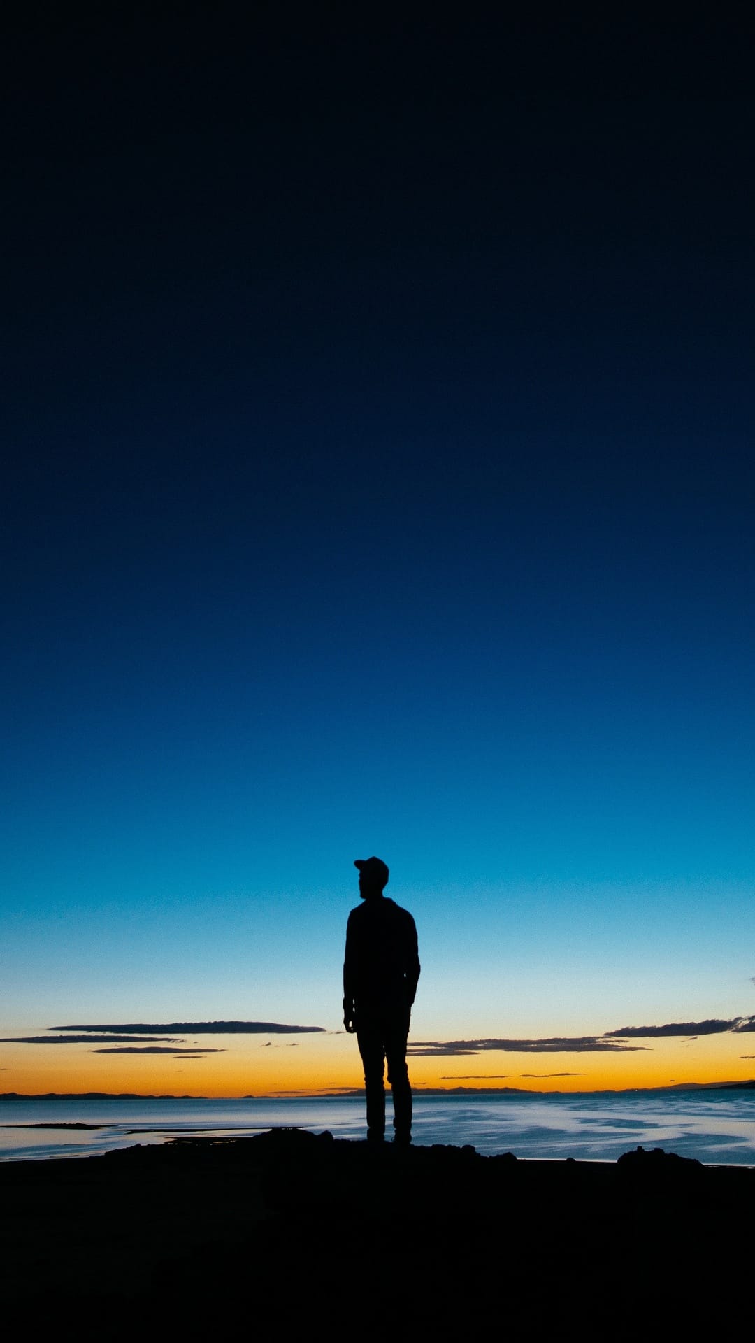Solitary person silhouetted against a gradient blue and orange sunset sky overlooking a misty coastal landscape.