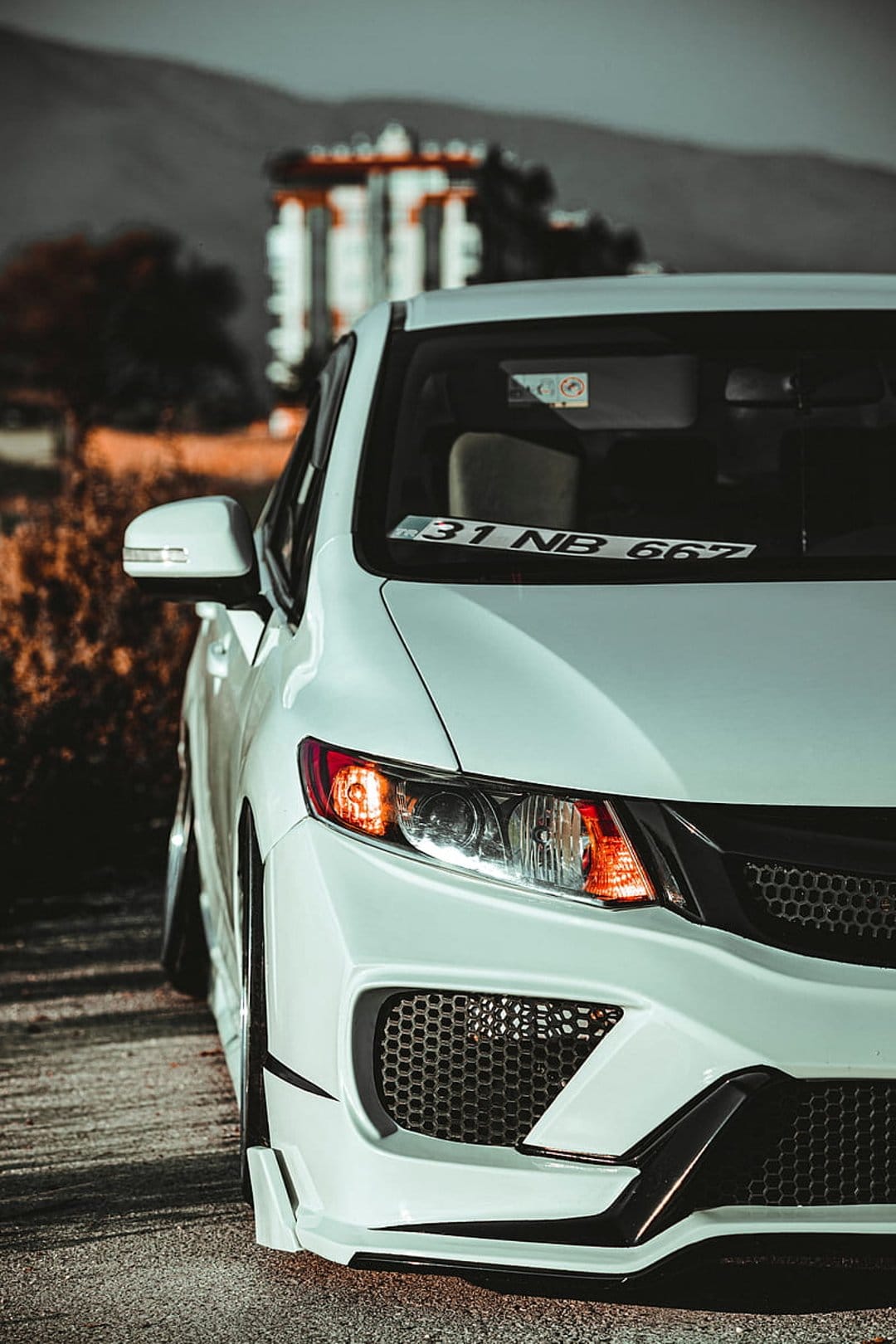 White Honda Civic RS with a custom front bumper and black mesh grilles parked on an asphalt road in daylight.