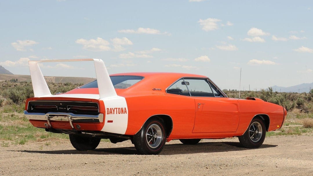Orange 1969 Dodge Charger Daytona with a tall white rear wing parked in a desert landscape under a blue sky.