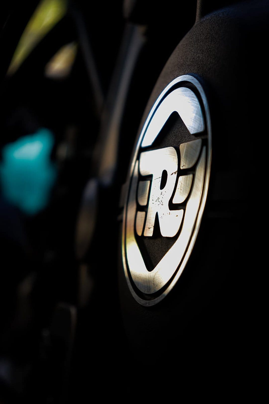 Royal Enfield silver winged logo on a dark textured motorcycle surface with a blurred black background.