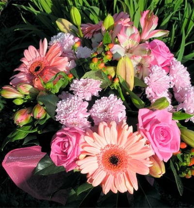 Pink gerbera daisies, roses, and carnations with green leaves and hypericum berries in a bright floral bouquet.