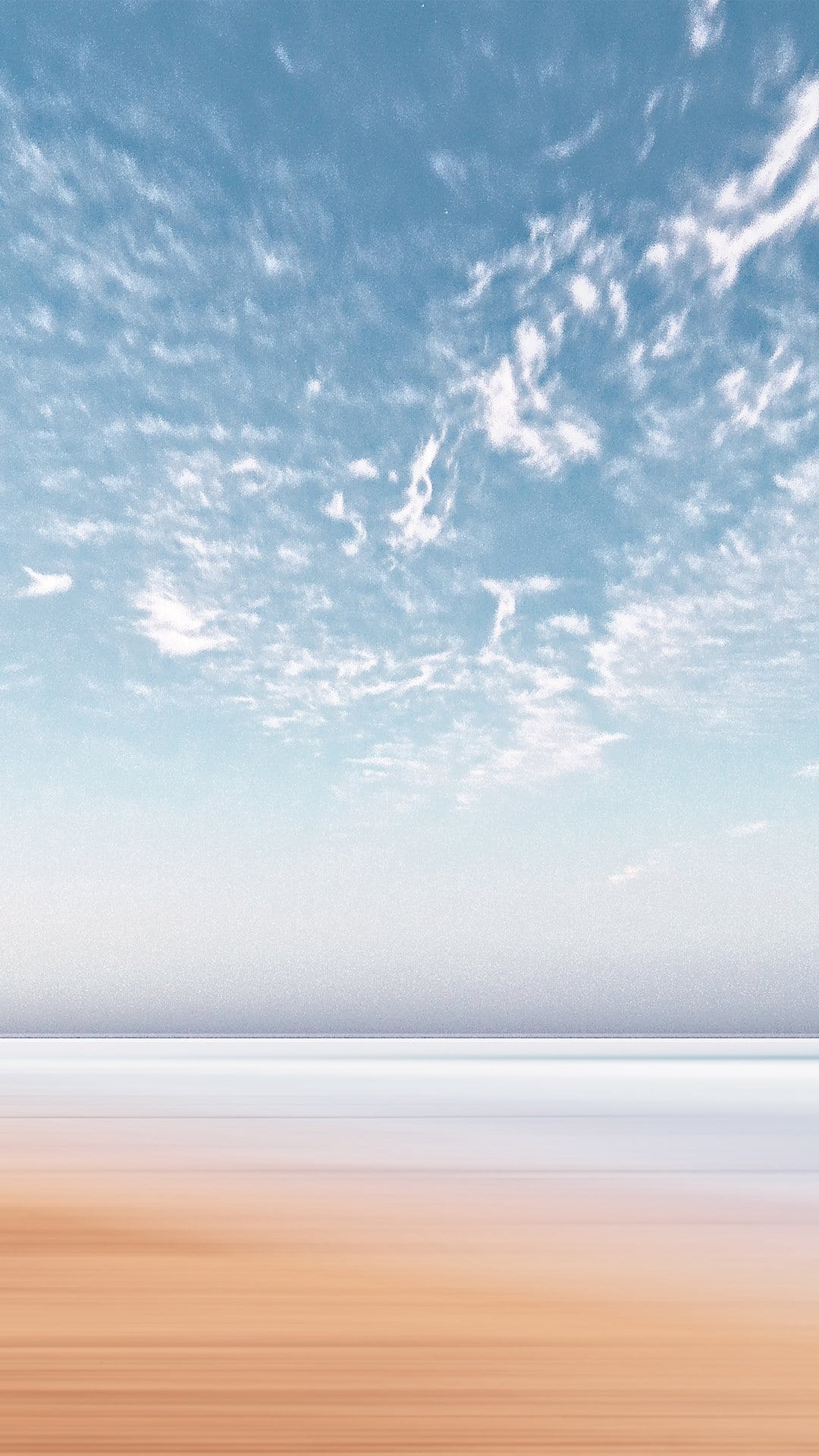 Cerulean sky with wispy clouds transitions into blurred white mist and streaked ochre sand dunes.
