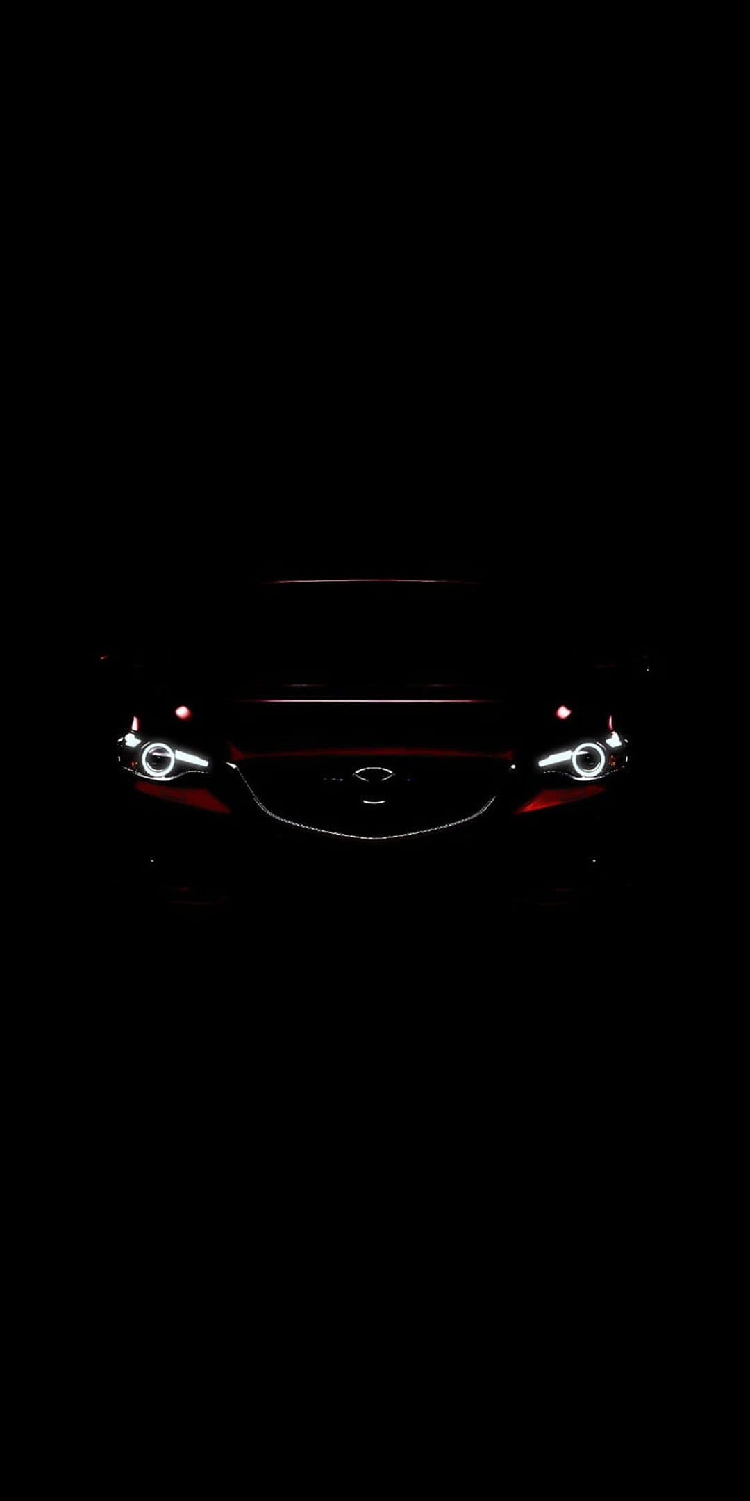 Red Mazda front grille and illuminated LED headlights positioned against a dark black background in portrait view.