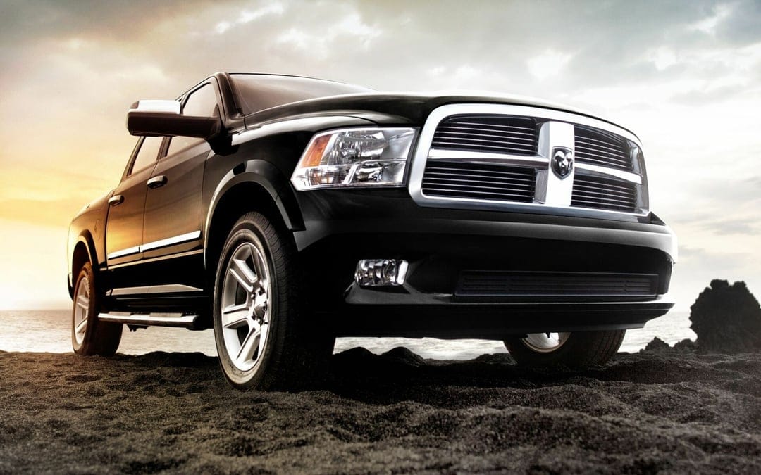 Black Dodge Ram 1500 truck parked on dark volcanic sand with a dramatic sunset sky and chrome grille.