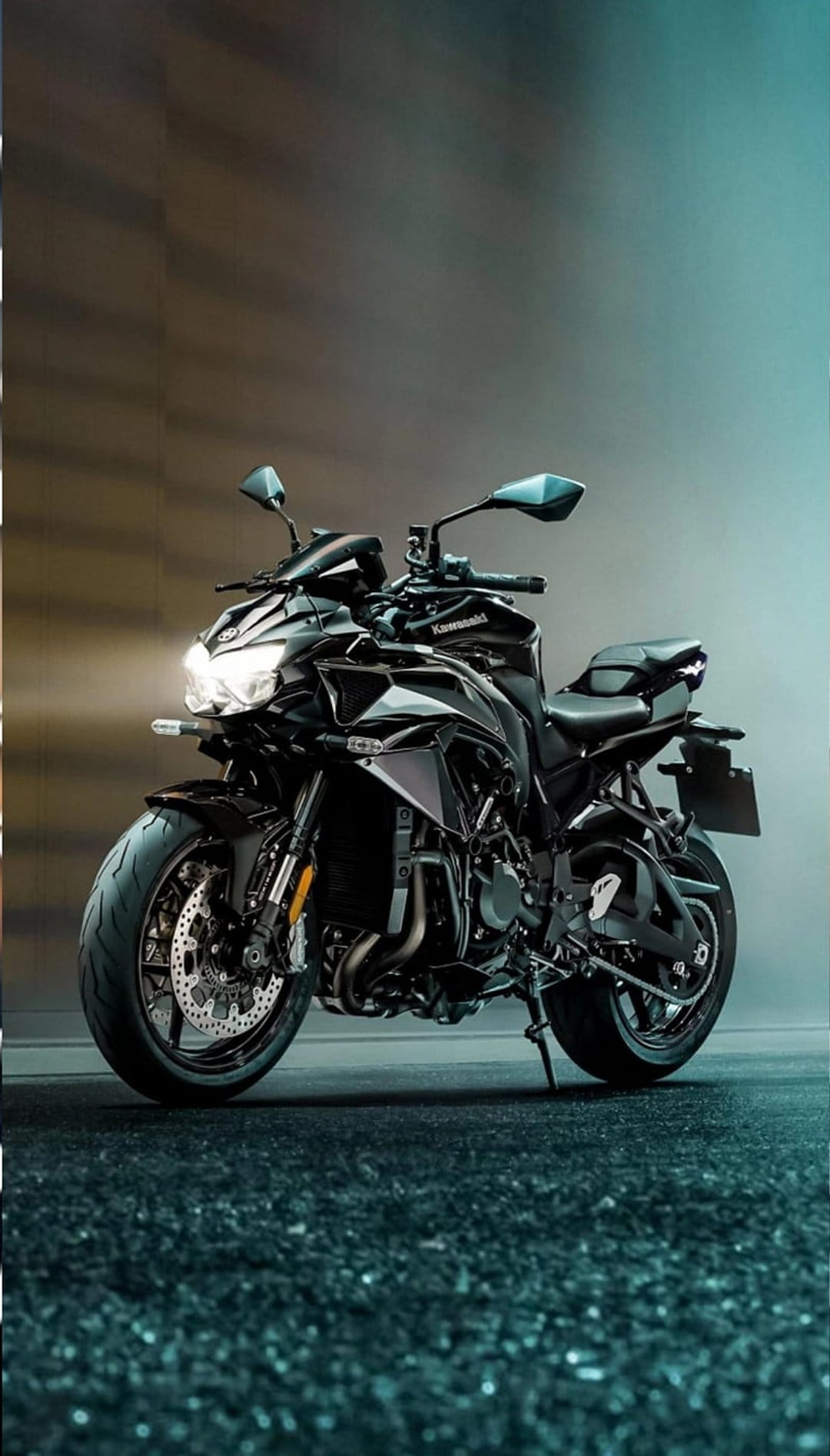 Black Kawasaki motorcycle with a lit headlight stands on a speckled dark floor against a teal and brown background.