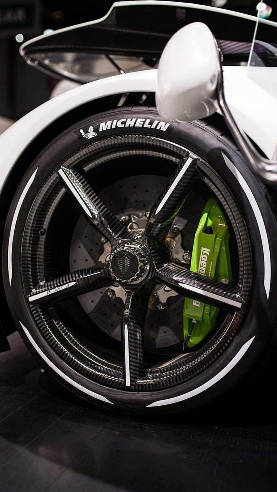 Koenigsegg carbon fiber wheel rim with a bright green brake caliper and white Michelin tire lettering close-up.