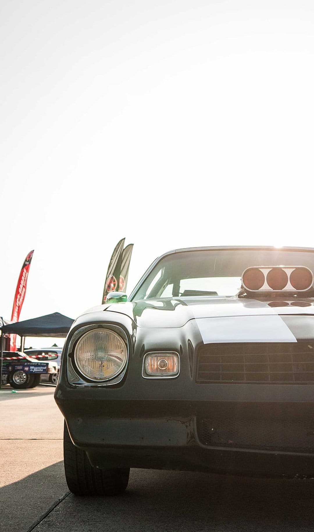 Black vintage Chevrolet Camaro with a white racing stripe and hood scoop parked outdoors at a low-angle view.