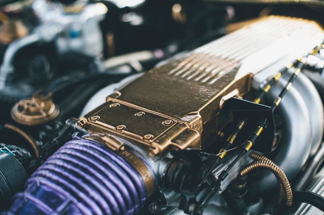 Gold supercharger assembly with purple intake piping and metallic engine components in a customized vehicle bay.