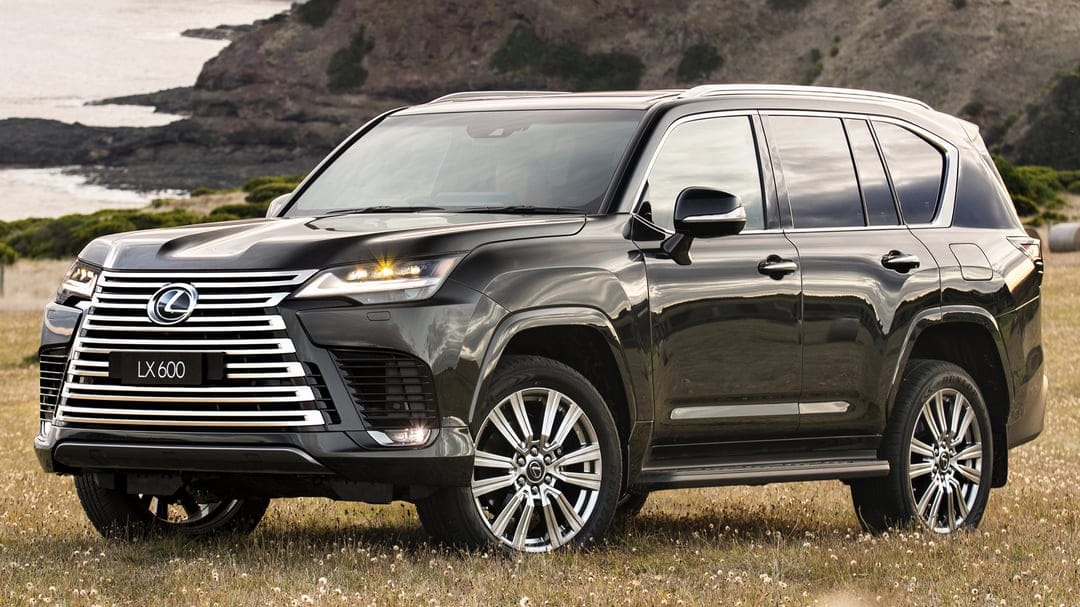 Black Lexus LX 600 SUV parked in a grassy field with coastal cliffs and the ocean in the background.