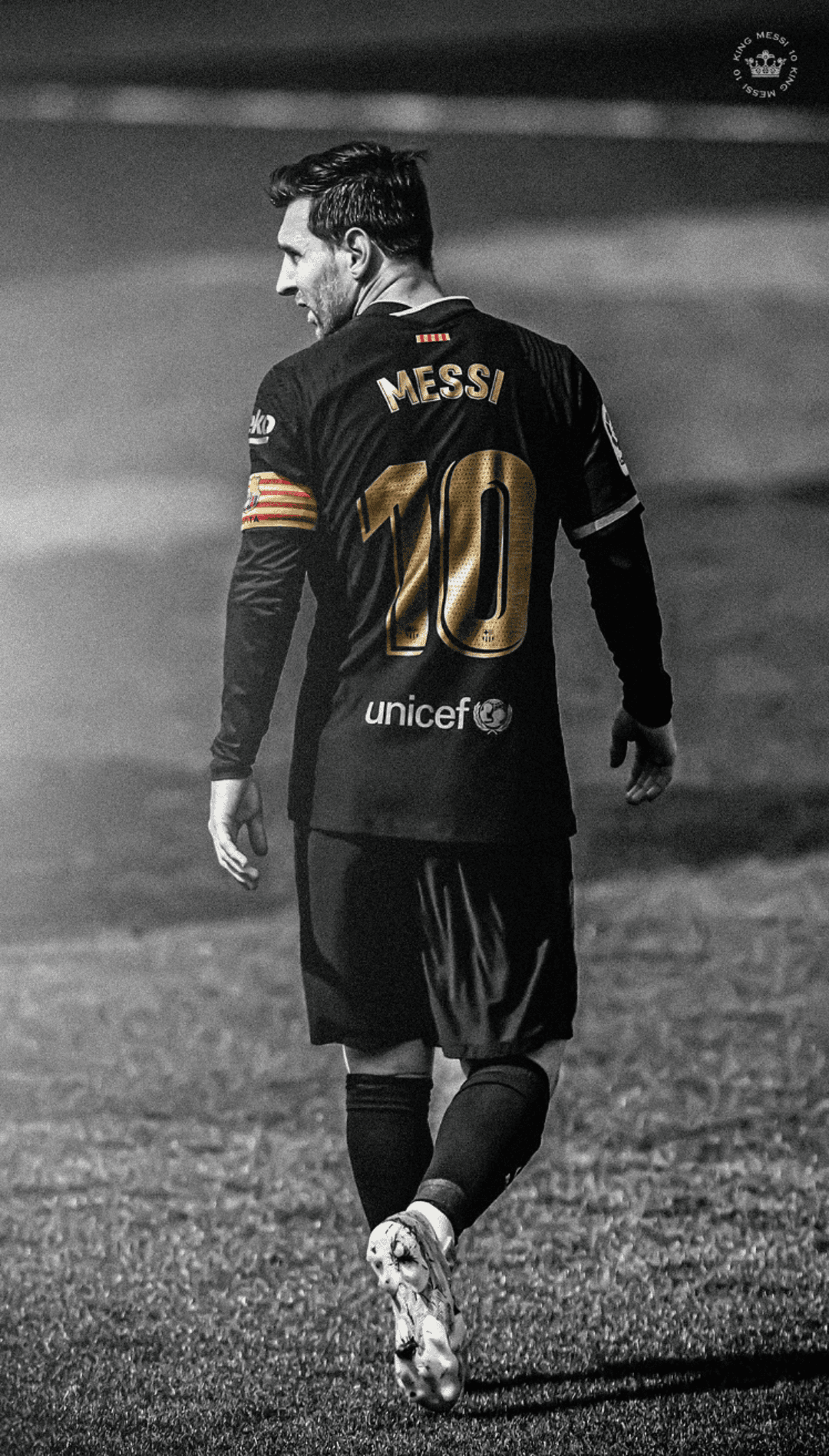 Lionel Messi seen from behind wearing a black and gold Barcelona jersey while standing on a grayscale pitch.