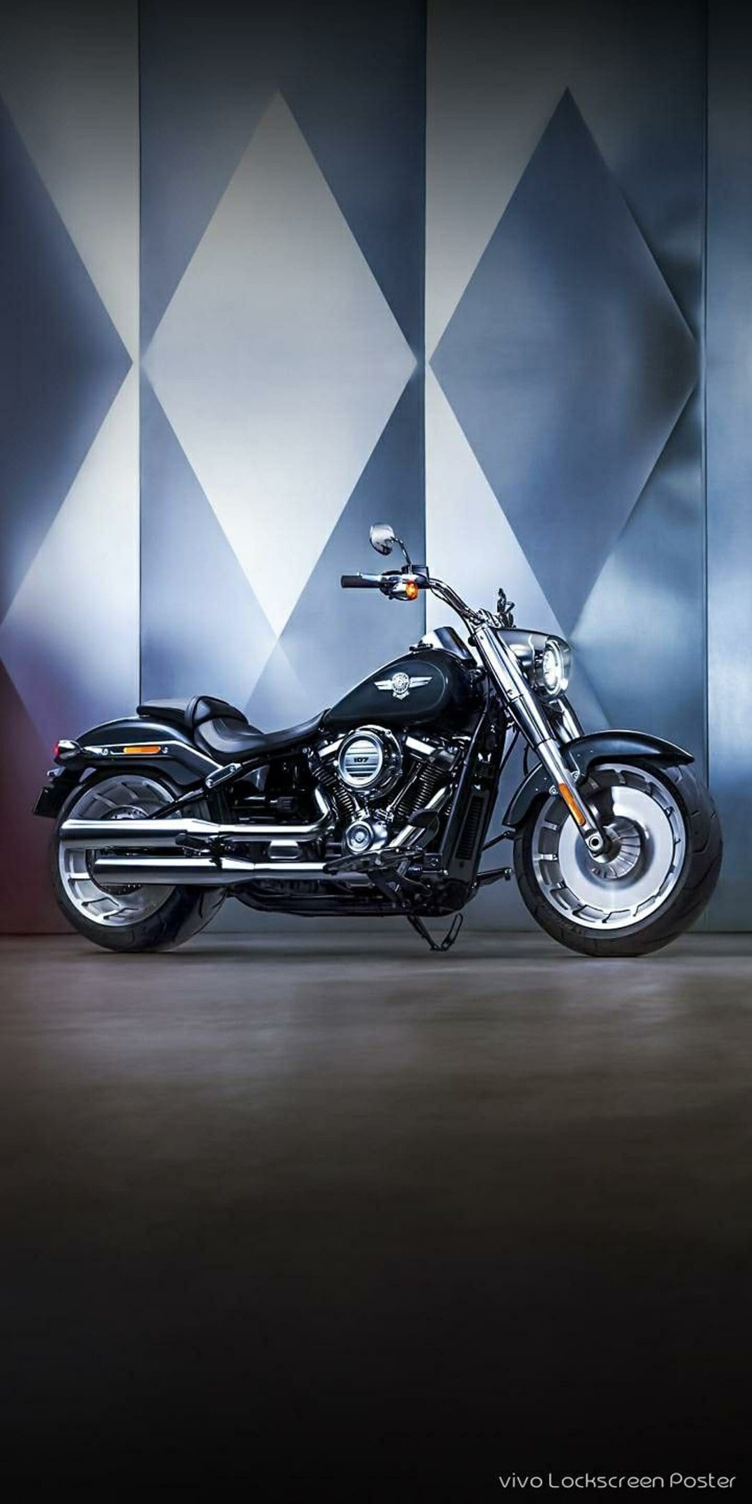 Harley-Davidson Fat Boy motorcycle parked in front of a modern wall with textured diamond-shaped metal panels.