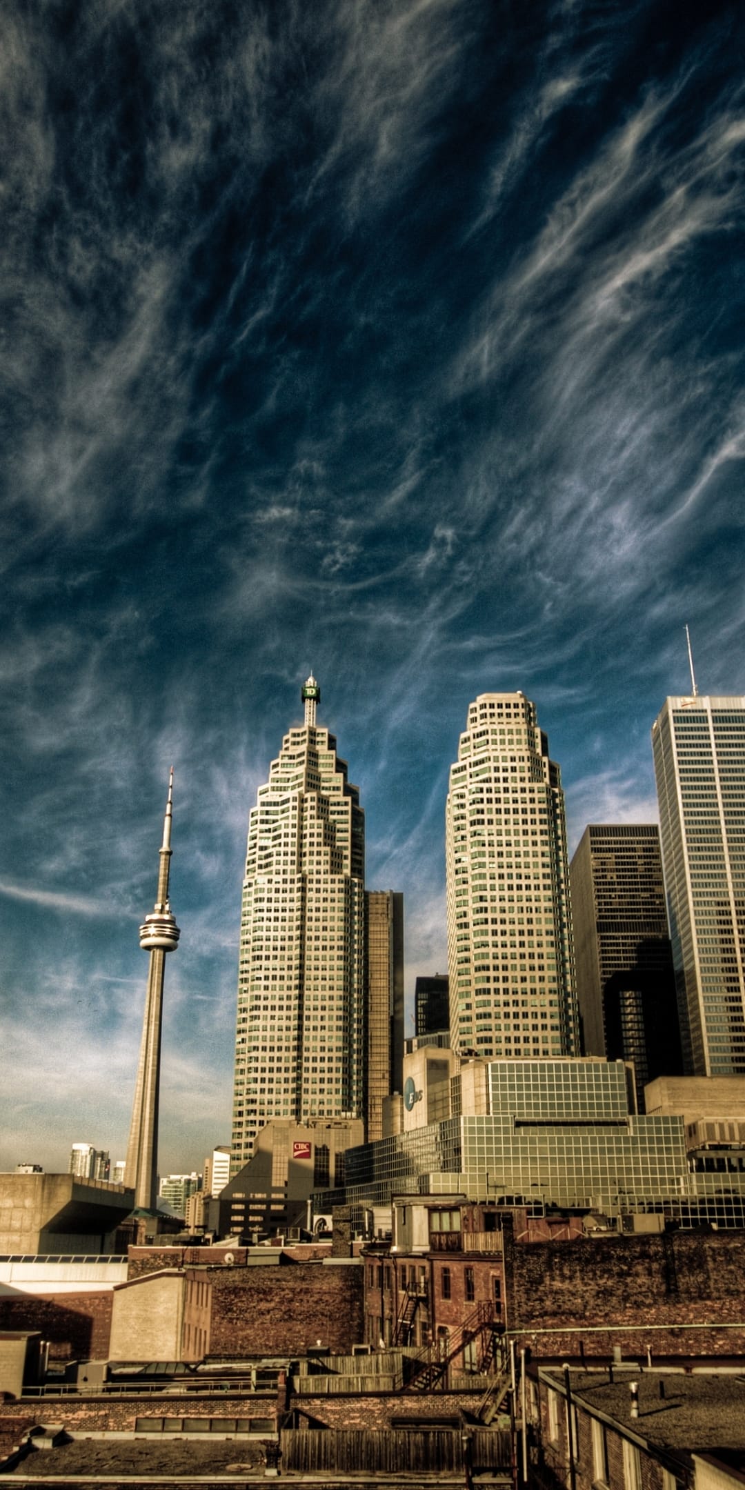 CN Tower and modern skyscrapers stand tall behind vintage brick buildings under a streaky, vibrant blue sky.