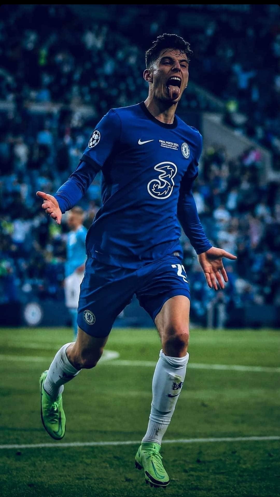 Kai Havertz celebrates a goal in a blue Chelsea jersey with arms out during a stadium football match.